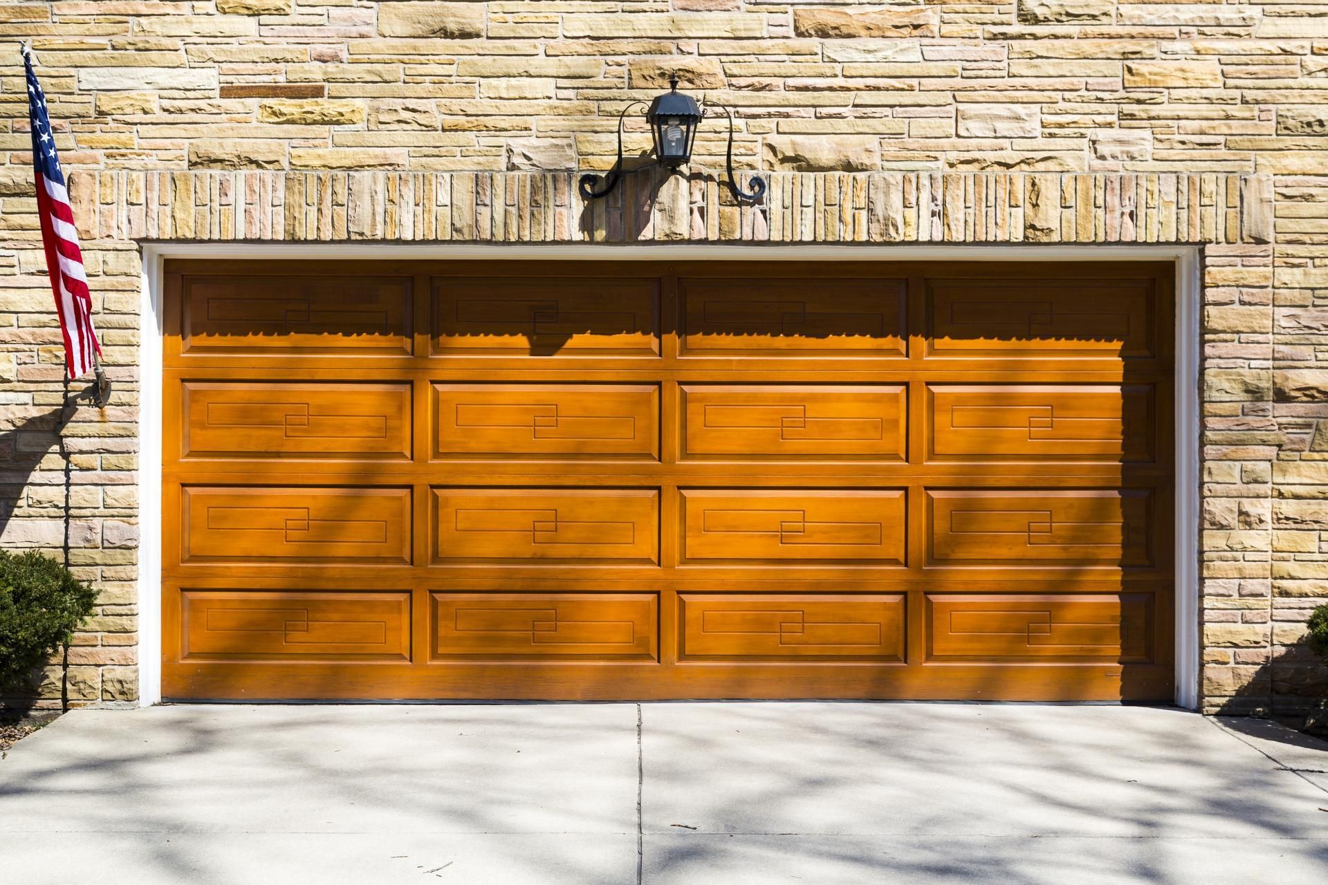 Brown garage door with light-colored brick exterior, an American flag, and concrete driveway.