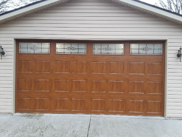 Brown garage door with decorative windows, beige siding, and concrete driveway.