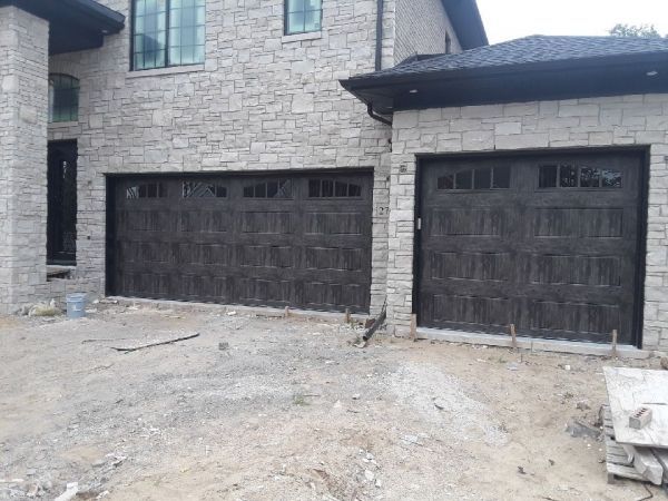 Two dark brown garage doors, set in stone facade, under a house with a stone exterior.