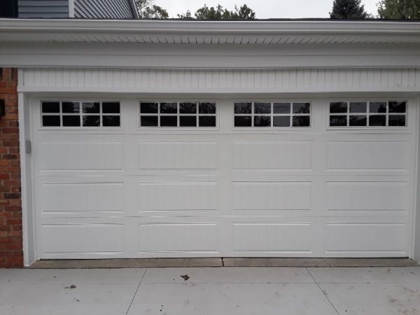 White garage door with windowed panels above, set in a white frame, with a concrete driveway.