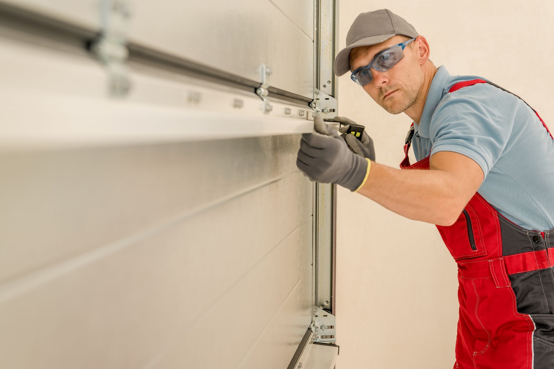 Man in safety gear repairing a white garage door, indoors.