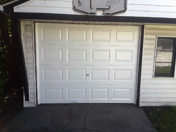 White garage door with basketball hoop above. Asphalt driveway and small window on the right.