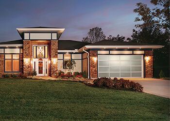 Modern home exterior at dusk, featuring a garage with a frosted glass door, brick accents, and a manicured lawn.