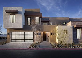 Modern home exterior with stucco and stone facade, glass garage door, and arid landscaping.