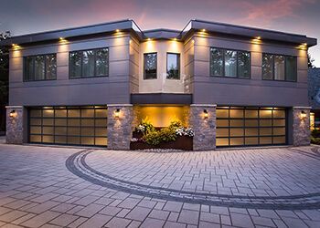 Modern house with two garage doors and a patterned driveway. Gray exterior with stone accents and built-in planters.