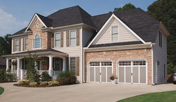 Two-story beige house with brick, and two-car garage. Beige garage doors, green lawn, blue sky.