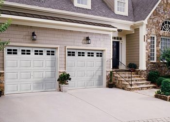 Two white garage doors on a light-colored house with stone accents, a driveway, and front steps.