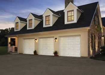 Three-car garage with white doors, tan siding, and a dark shingle roof with dormer windows.