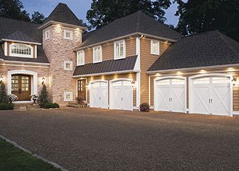 Exterior view of a large house with a stone tower and three white garage doors.