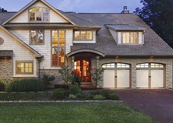 Two-story house with stone facade, arched doorway, and two garage doors. Landscaped front yard and driveway.