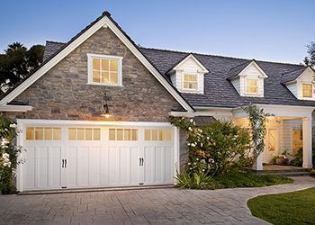 White garage door on a stone-faced house. Driveway and landscaping.