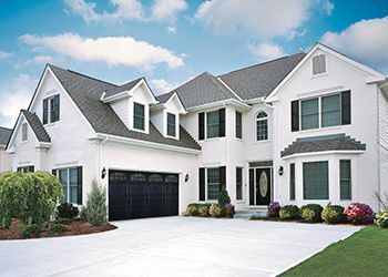 White two-story house with dark garage door, black shutters, and clear blue sky.