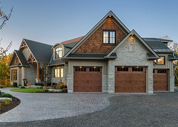 Large house with stone facade, brown garage doors, and a winding driveway.