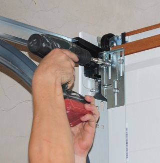 Person using a drill to install hardware on a garage door track.