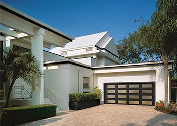 Modern white house with a black framed, glass-paned garage door; paved driveway and blue sky.