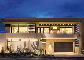 Modern two-story house at dusk, featuring large windows, a garage, and desert landscaping.