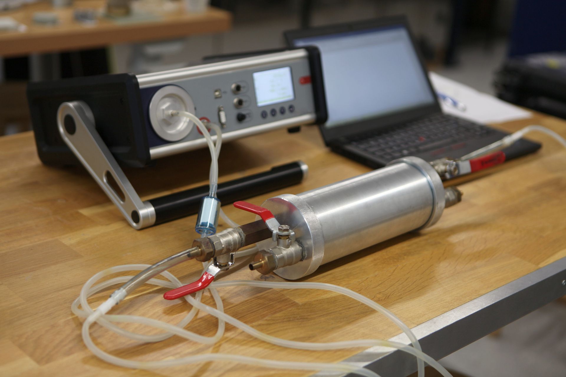 A silver cylinder with tubes connected to a machine and a laptop on a table.