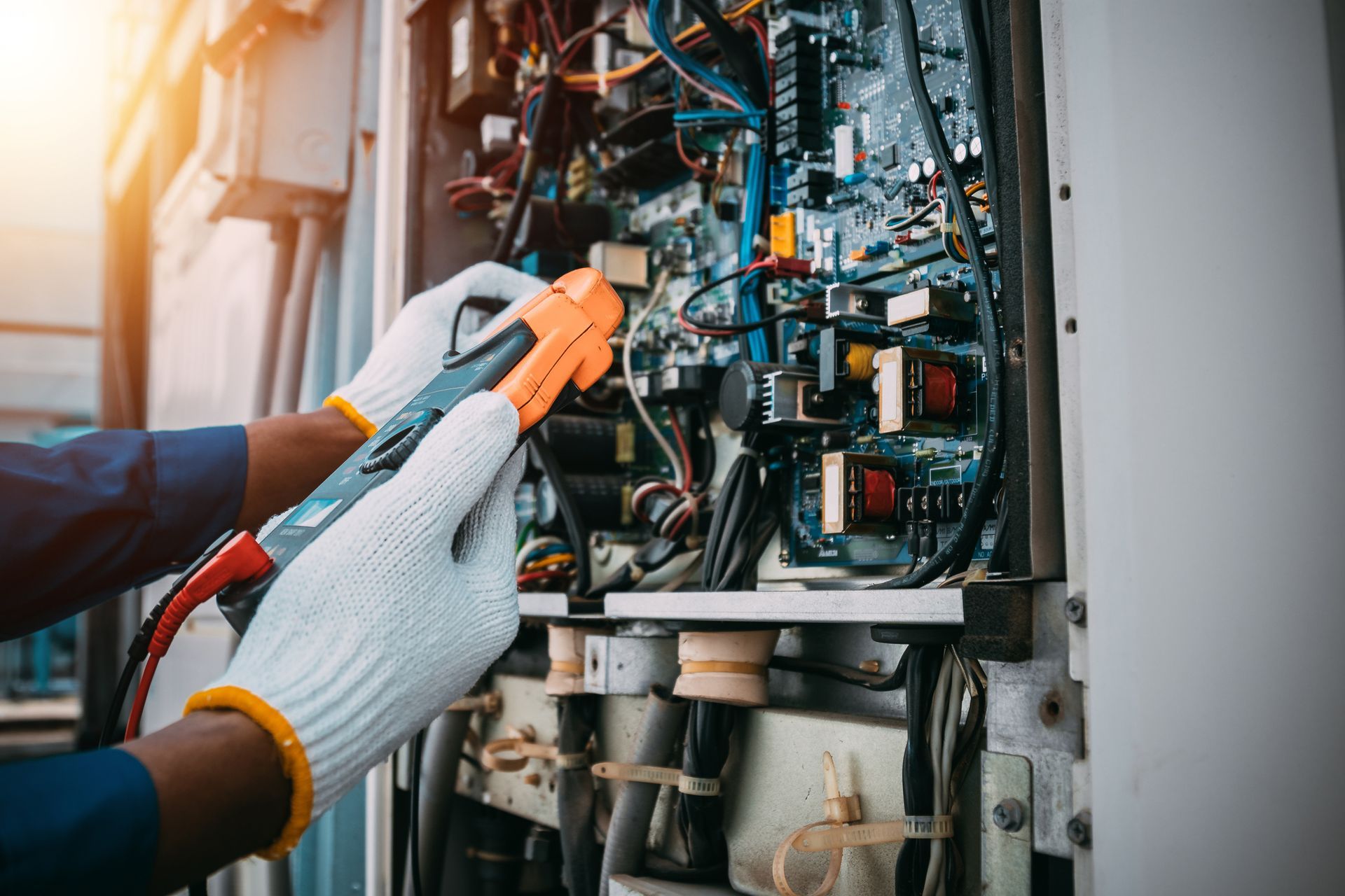 A person wearing gloves is using a multimeter to test electrical components inside a panel.