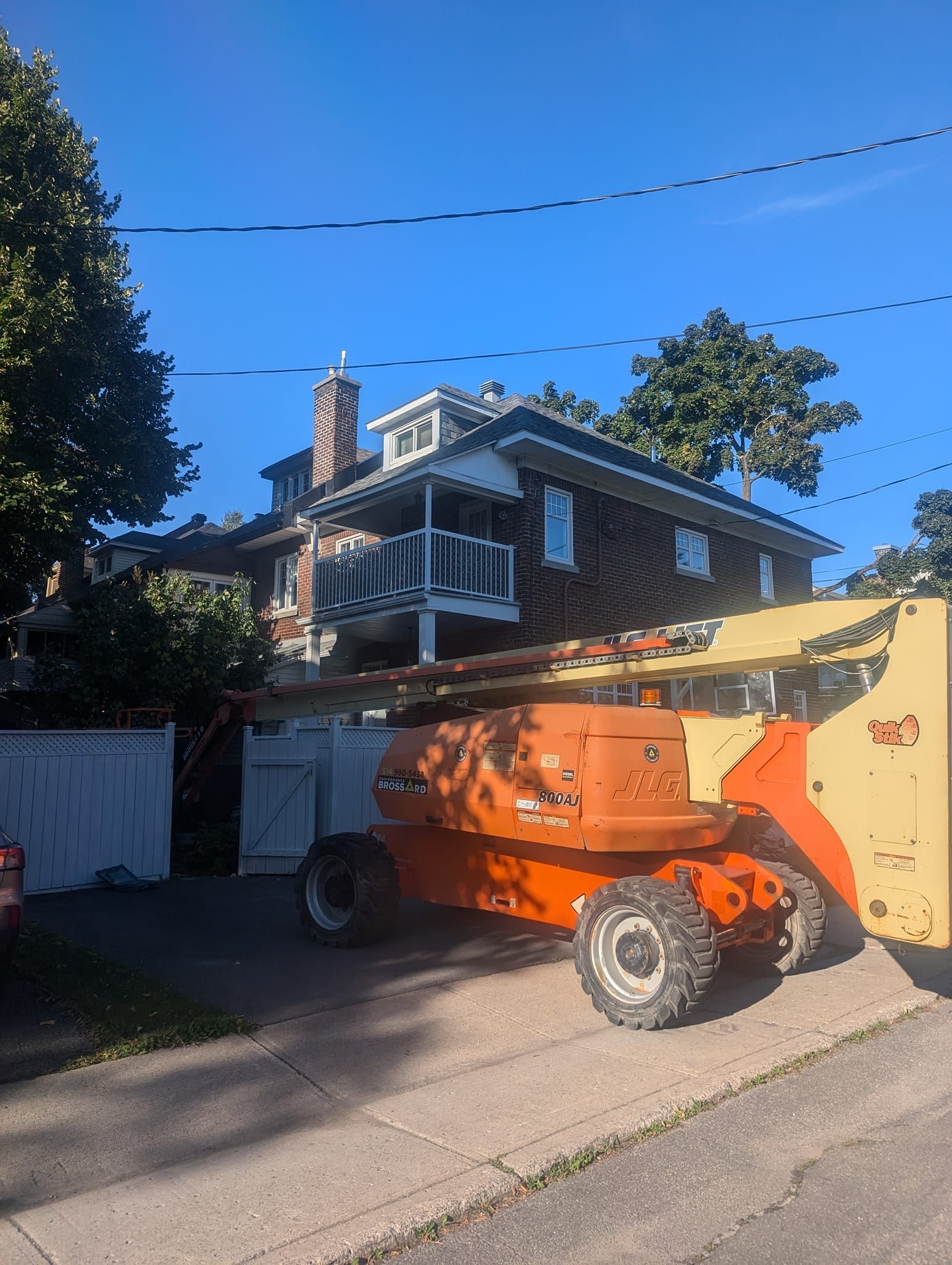 Un gros tracteur orange est garé devant une grande maison.