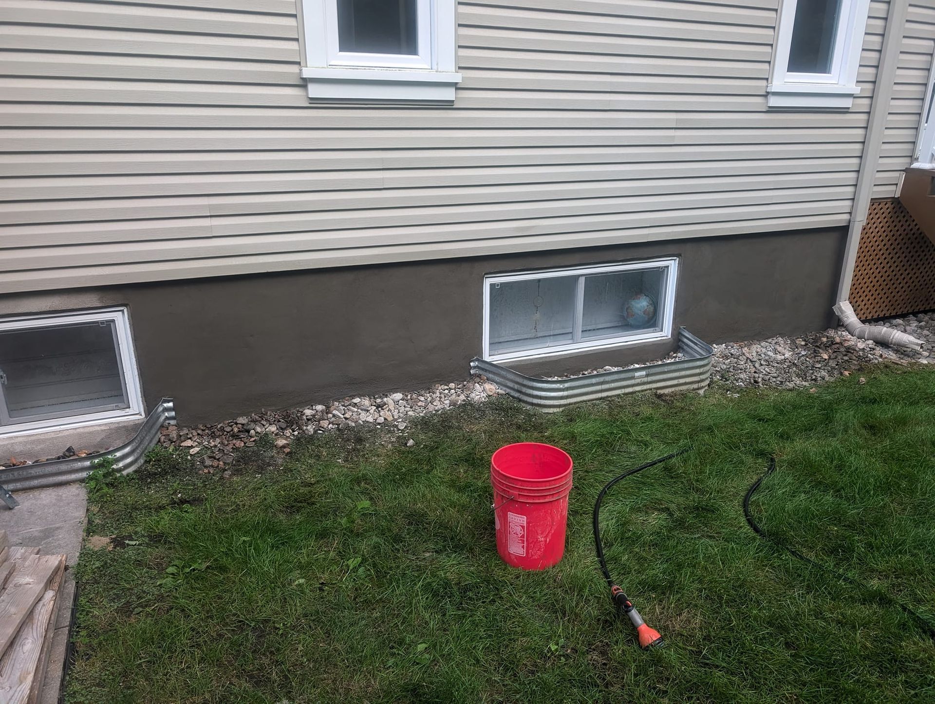 Un seau rouge est posé dans l'herbe devant une maison.