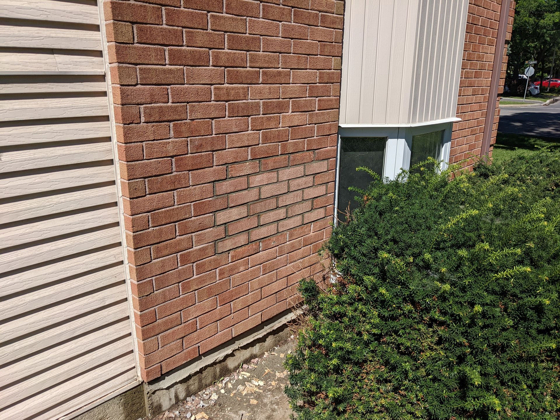 Un bâtiment en briques avec une fenêtre et un buisson devant.