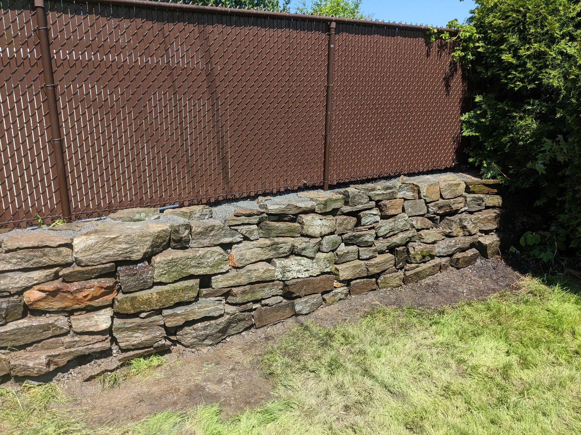 Un mur de pierre avec une clôture derrière dans une cour arrière.