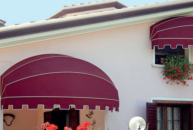 Esterno della casa con tende da sole color bordeaux e una piccola fioriera sotto la finestra superiore.