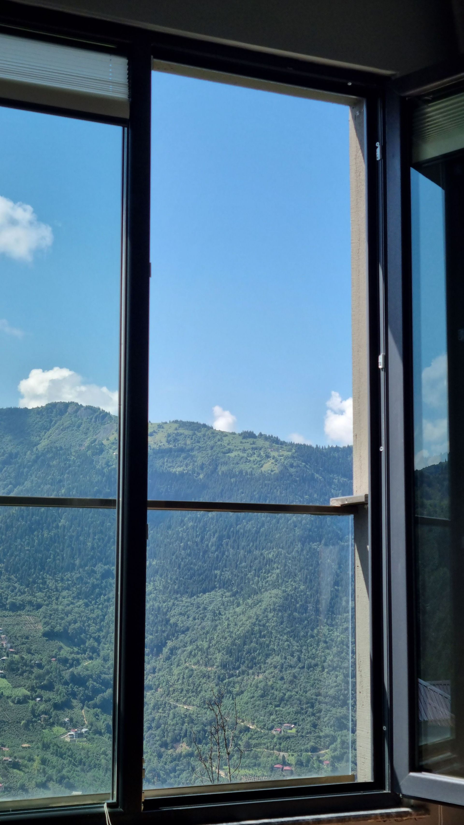 Finestra aperta che incornicia il cielo azzurro, le nuvole e le montagne boscose all'esterno