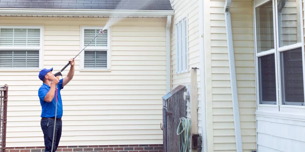 A man is cleaning the side of a house with a high pressure washer.