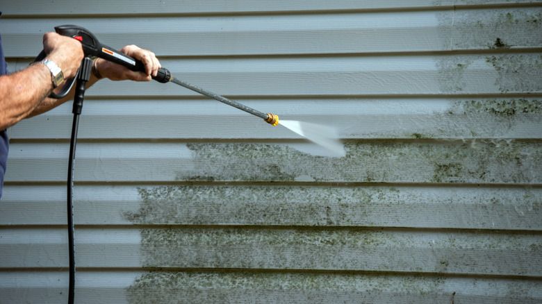 A man is using a high pressure washer to clean a house 's siding.