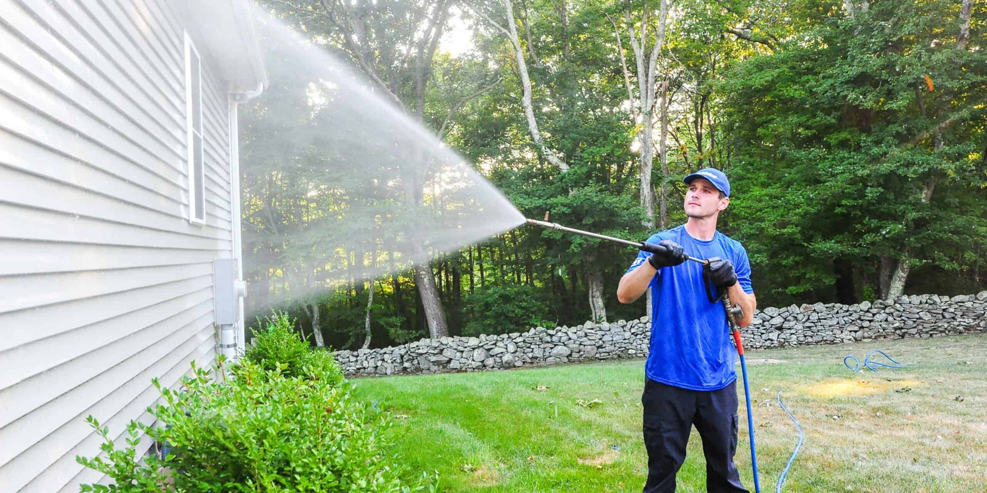 A man is cleaning the side of a house with a pressure washer.