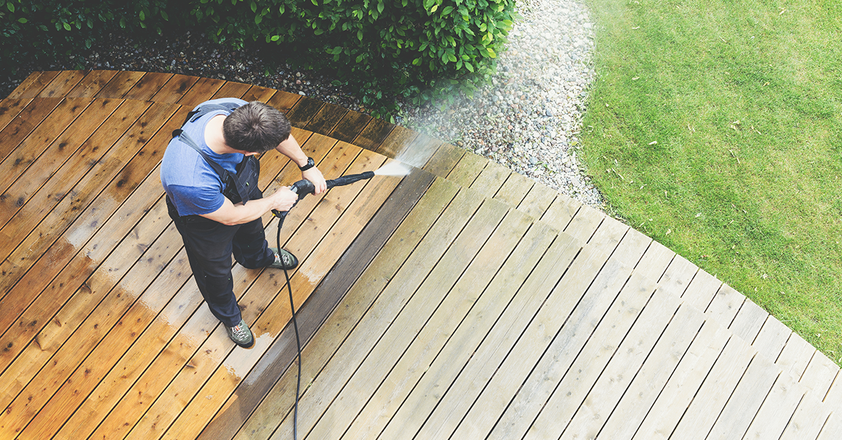 A man is cleaning a wooden deck with a high pressure washer.