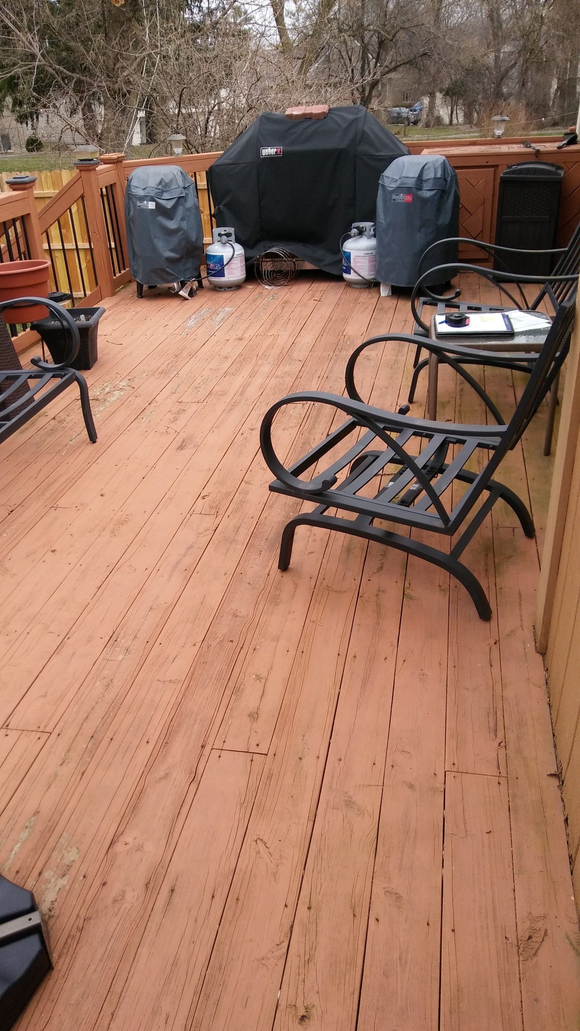 A wooden deck with a grill and chairs on it.