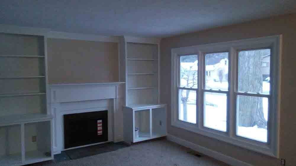 An empty living room with a fireplace , shelves , and windows.