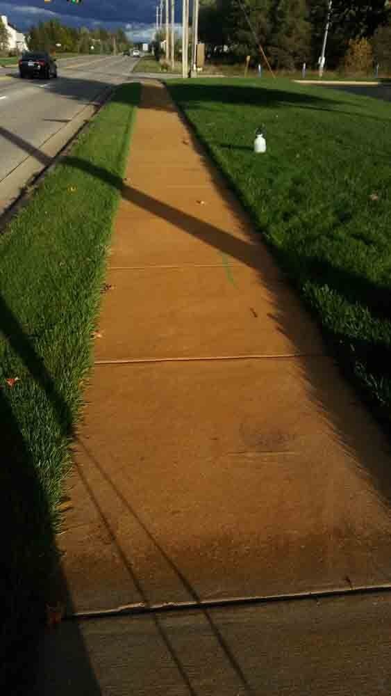 A sidewalk leading to a grassy field next to a road.