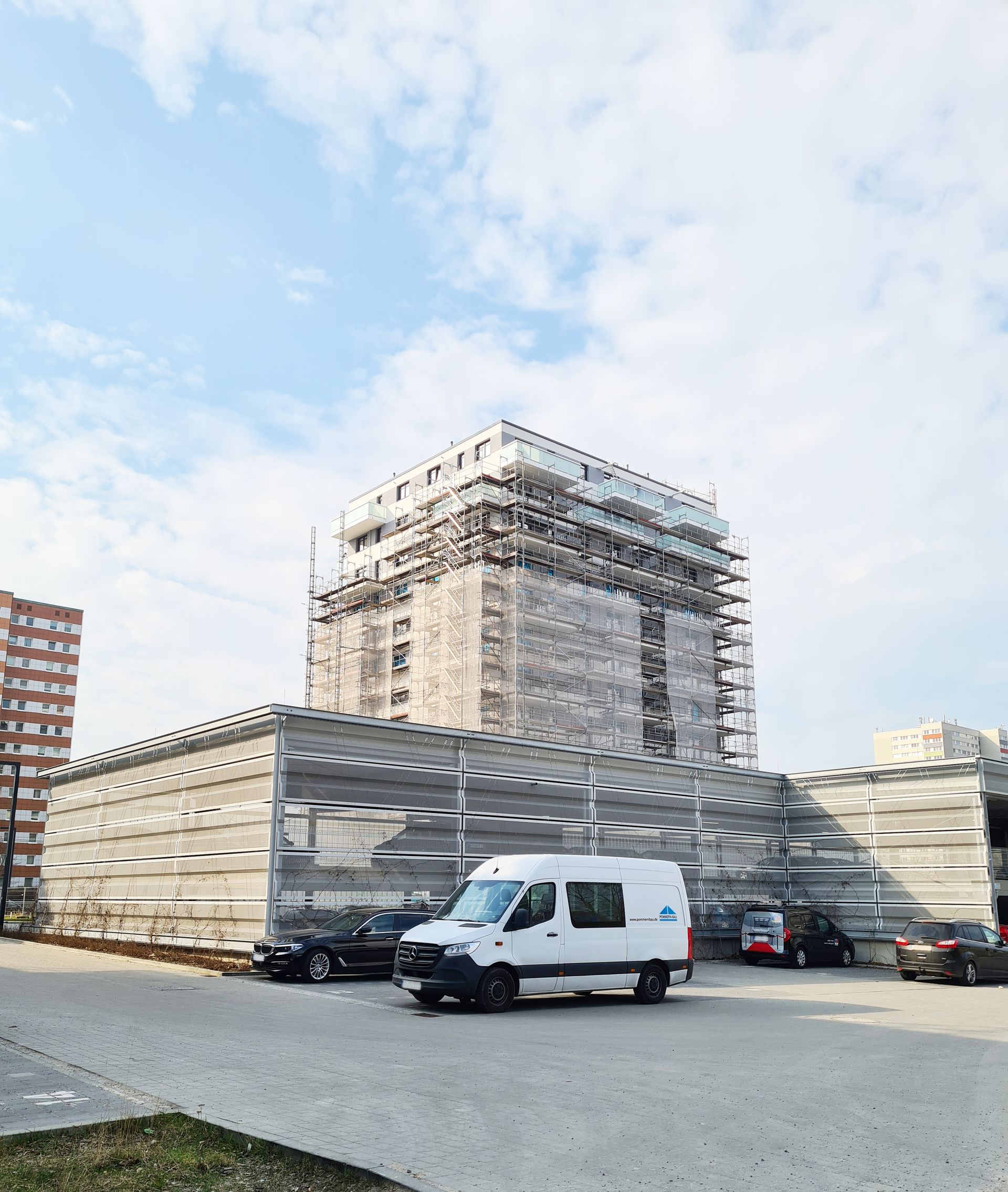 Ein eingerüsteter hoher Neubau eines Mehrfamilienhauses mit einem Fahrzeug von Pommern-Bau im Vordergrund.