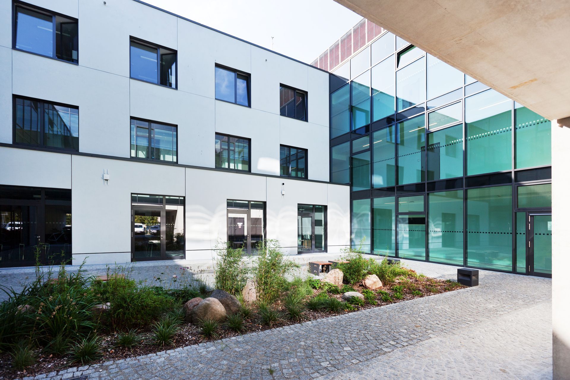 Blick auf eine weiße abgesetzte Gebäudewand mit vielen Fenstern und eine Glasfront