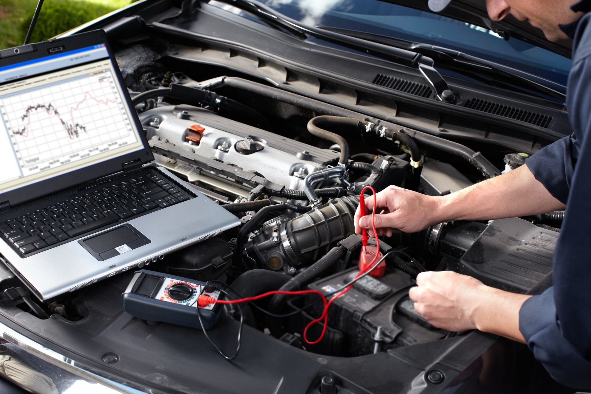 A cropped view of a car mechanic working in an auto repair shop while using a laptop for diagnostics.