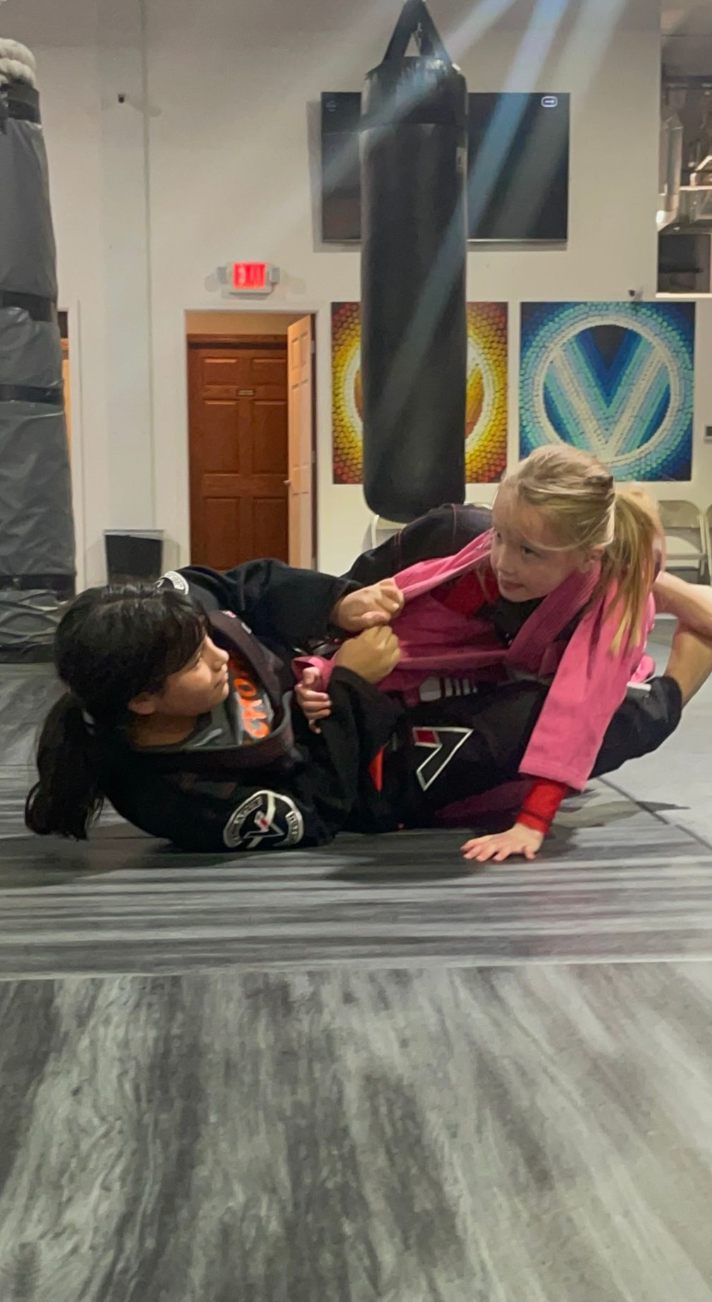 A boy and a girl are wrestling on a mat in a gym.
