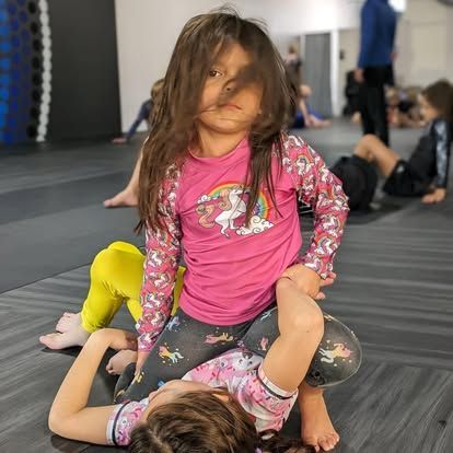 Two little girls are wrestling on a mat in a gym.
