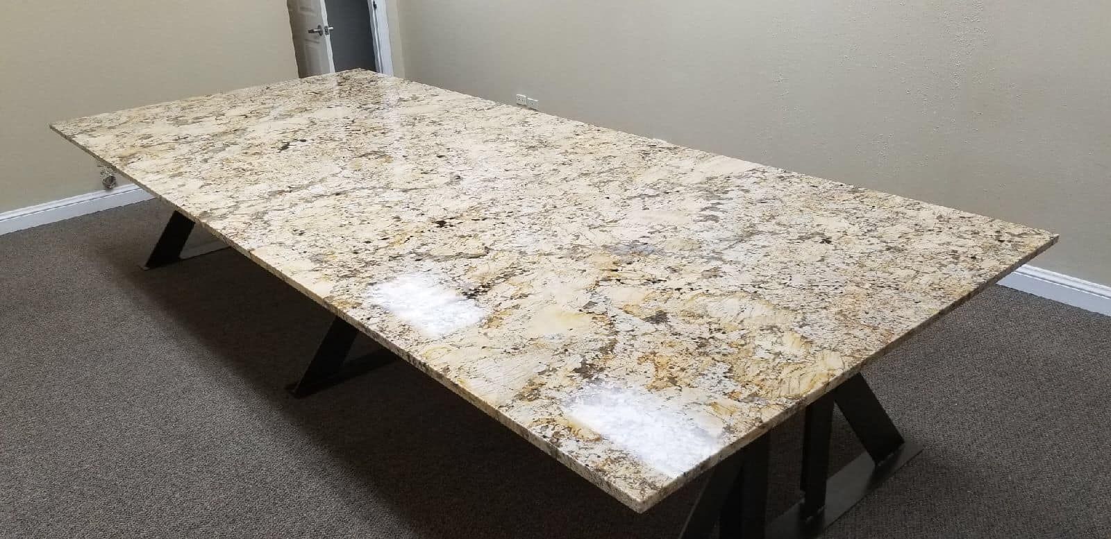 A granite table with brown and beige patterns stands on black legs in a room with beige walls and carpet.