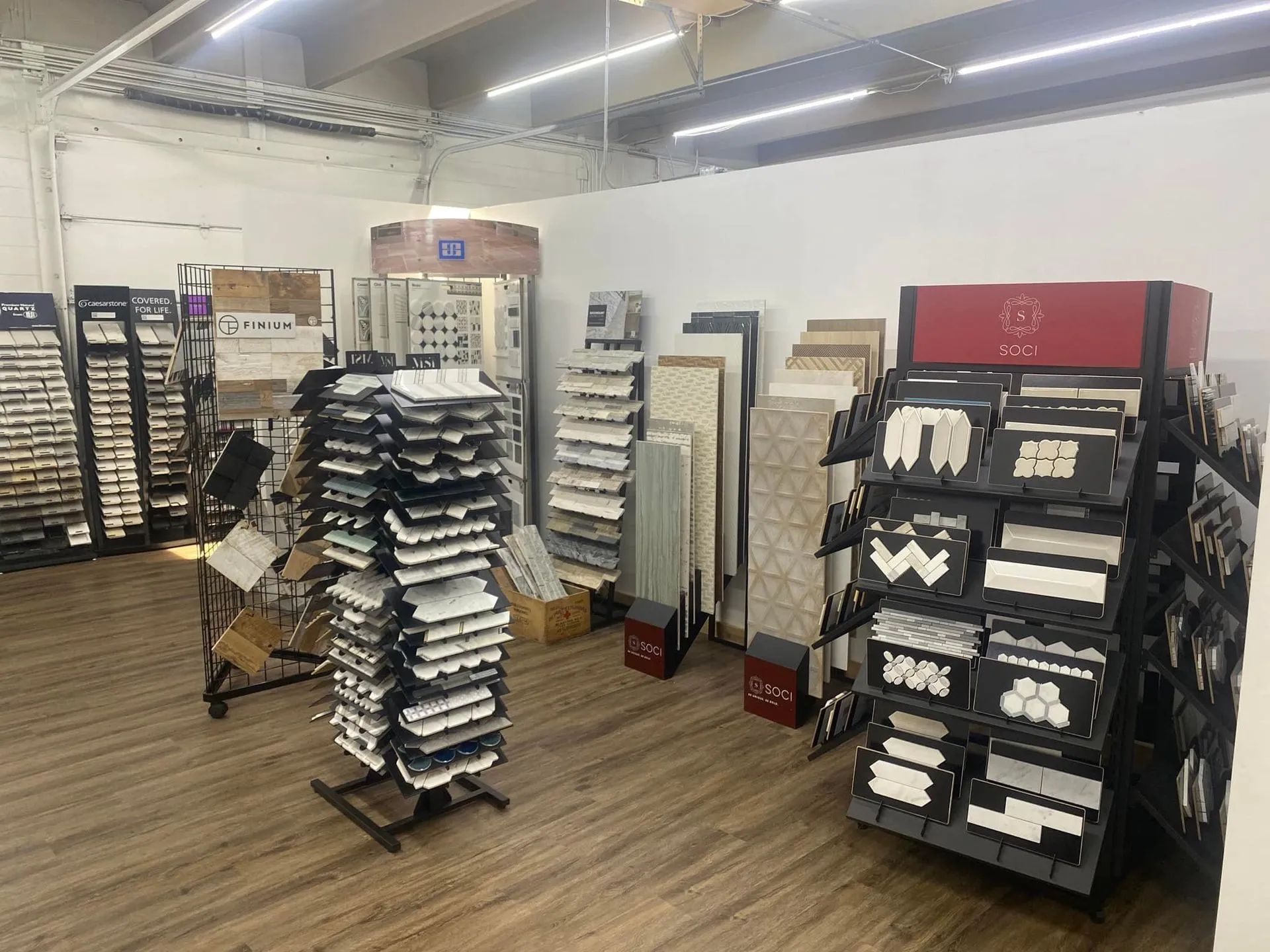 Warehouse aisle with stacks of labeled display racks and trays under bright overhead lights