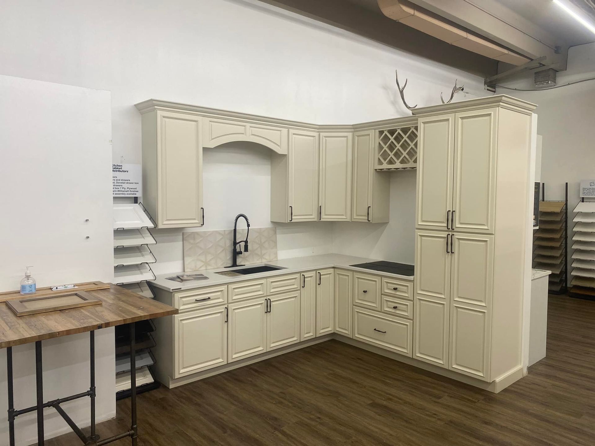 Cream-colored kitchen cabinets with black sink and appliances; dark wood floor, butcher block table; showroom.