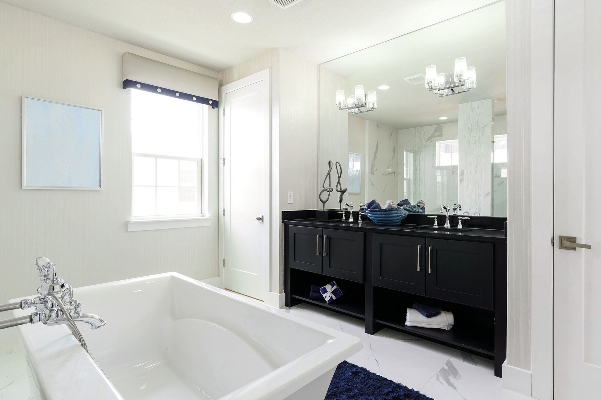 Bright white bathroom with a tub, dark vanity, large mirror, and window.