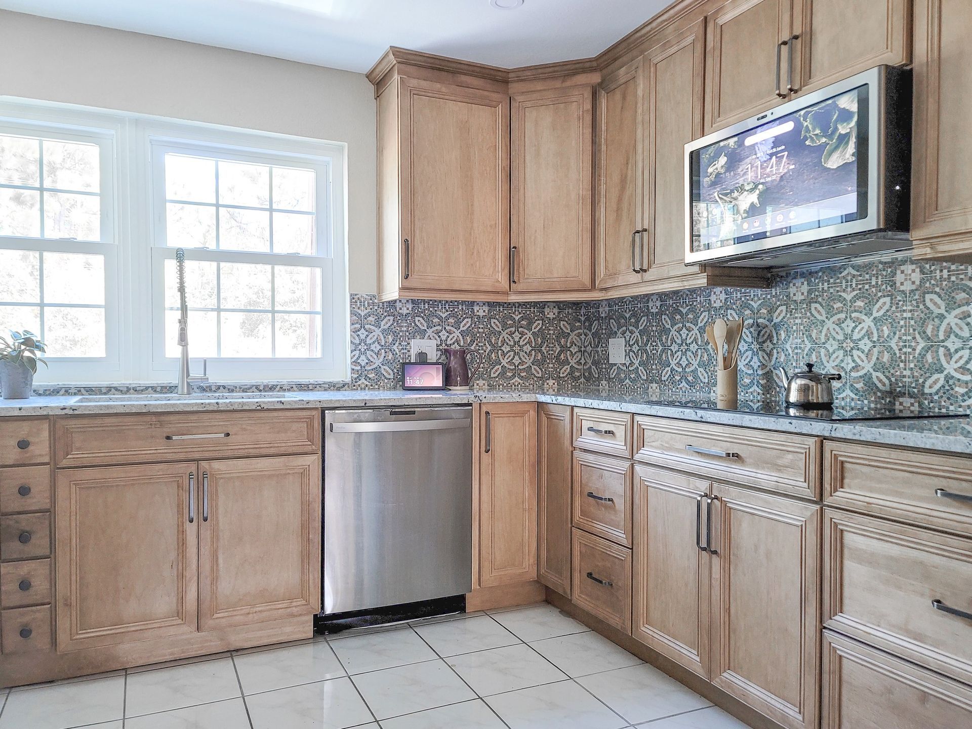 Kitchen with light wood cabinets, stainless steel appliances, and decorative backsplash tiles.
