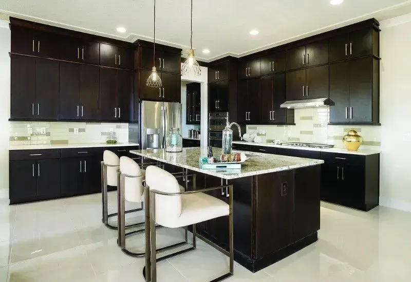 Dark wood kitchen with island, stainless steel appliances, and white countertop. Three bar stools at island.