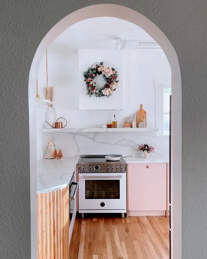 Kitchen with pink cabinets, white stove, marble countertop, and a floral wreath.