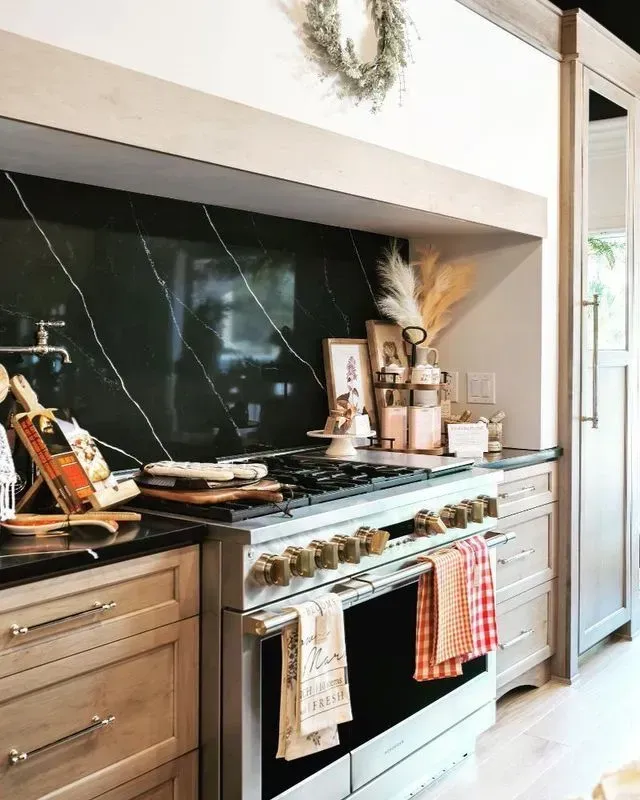 Kitchen with black marble backsplash, stainless steel range, light wood cabinets, and decor.
