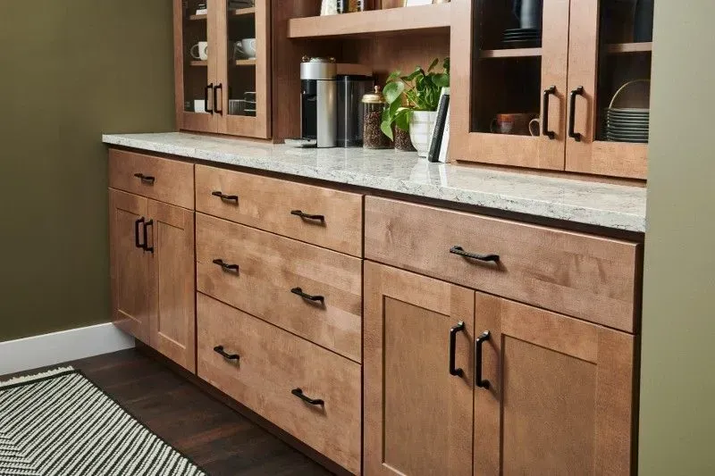 Light wood kitchen cabinets with black handles, white countertop, and green wall.