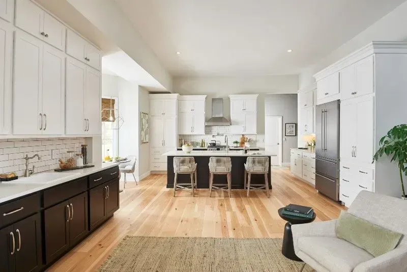 Bright, modern kitchen with white and dark cabinets, island with stools, and light wood flooring.